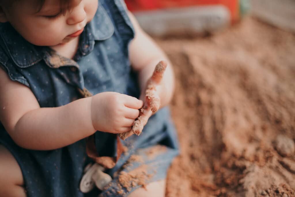 Baby Girl With Dirty Hands Playing With Sand, Possibly Catching Worms From Dog Feces