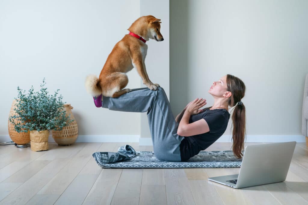 Young Woman In Yoga Position Balancing With Her Dog