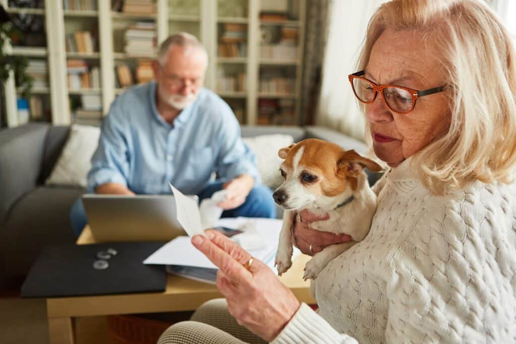 Worried Senior Woman Checking Expenses And Receipts With Man Doing Accounting In Background